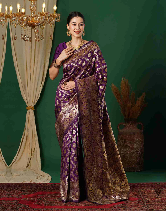 Woman in a purple and gold saree standing in a decorated room with a chandelier and plant.